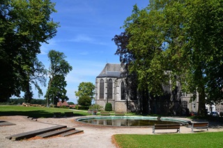 Stadspark met in de buurt de Sint-Urmaruskerk in Binche onder een stralend blauwe hemel.