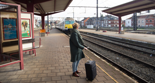 Een vrouw met haar valies wacht op het perron op de aankomende trein. 